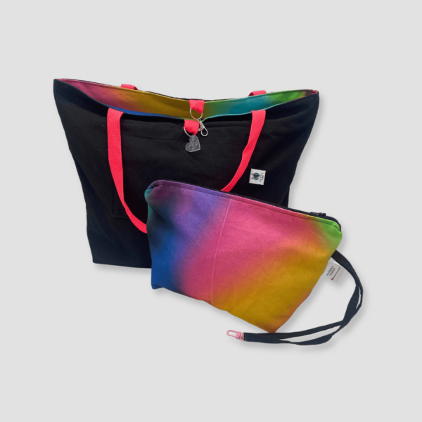 Bolso y neceser de loneta gradiente, reversible con cara interna en color negro y cara externa con estampado azul, amarillo, verde, rosa, rosa y asas de algodón en color rosa.